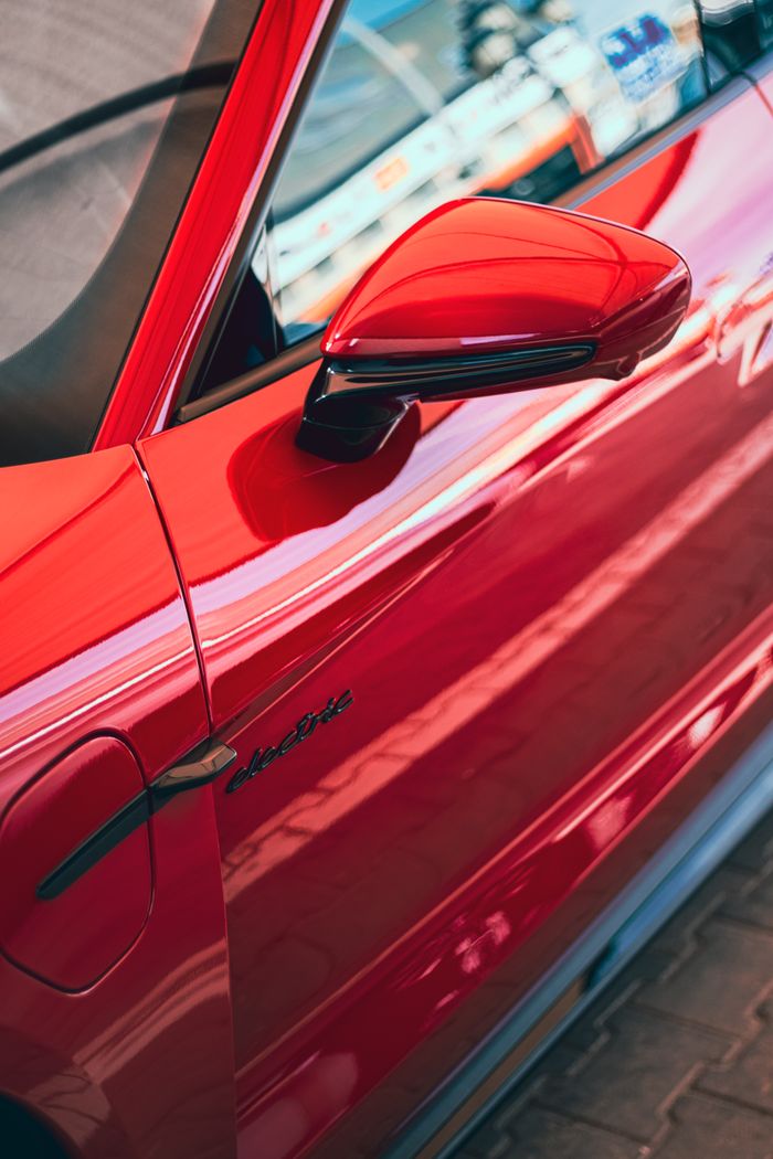 our-story-01 A vibrant red sports car door with sleek lines and a shiny mirror, capturing modern automotive design.